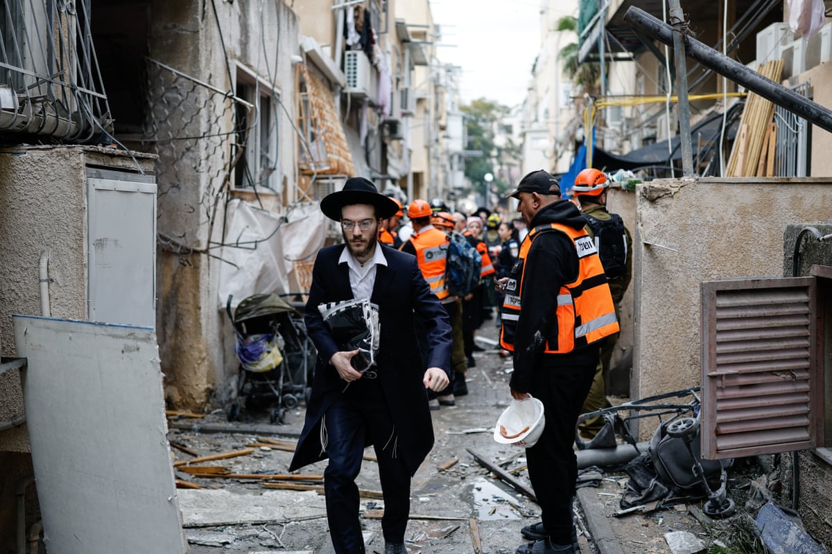 People and emergency walkers walk through a debris-strewn street.