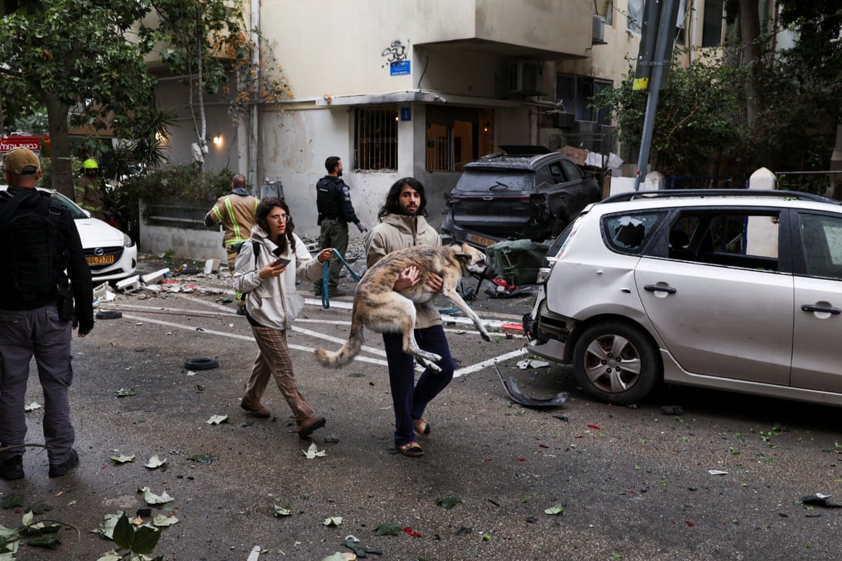 A man carries a dog through a street littered with debris. 