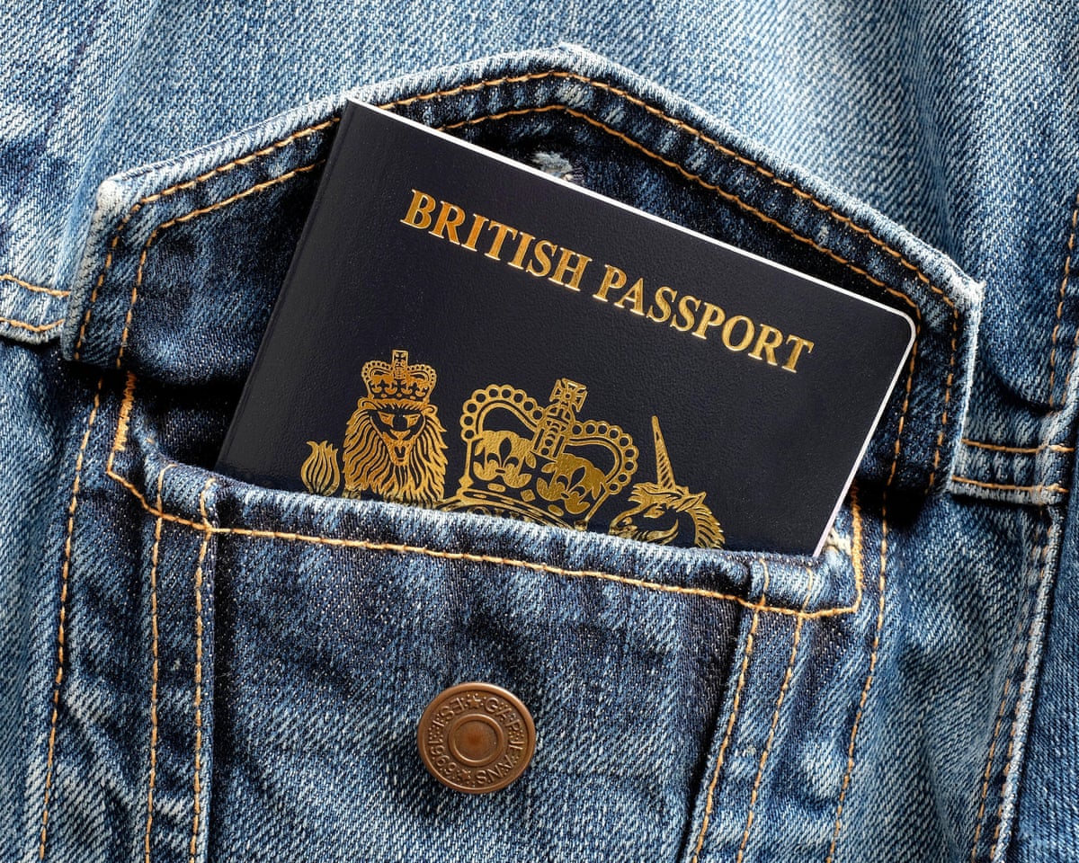 A blue British passport pokes out of a blue denim jacket pocket