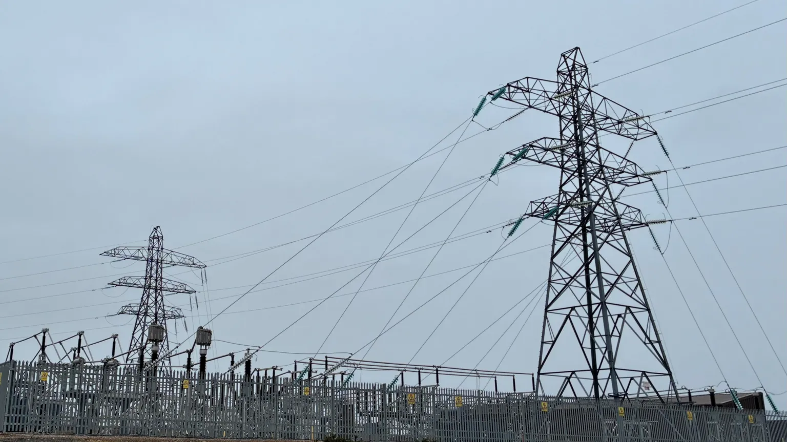 Spittal substation, Caithness - Two large electricity pylons and multiple power lines rise above a fenced electrical substation under an overcast sky.