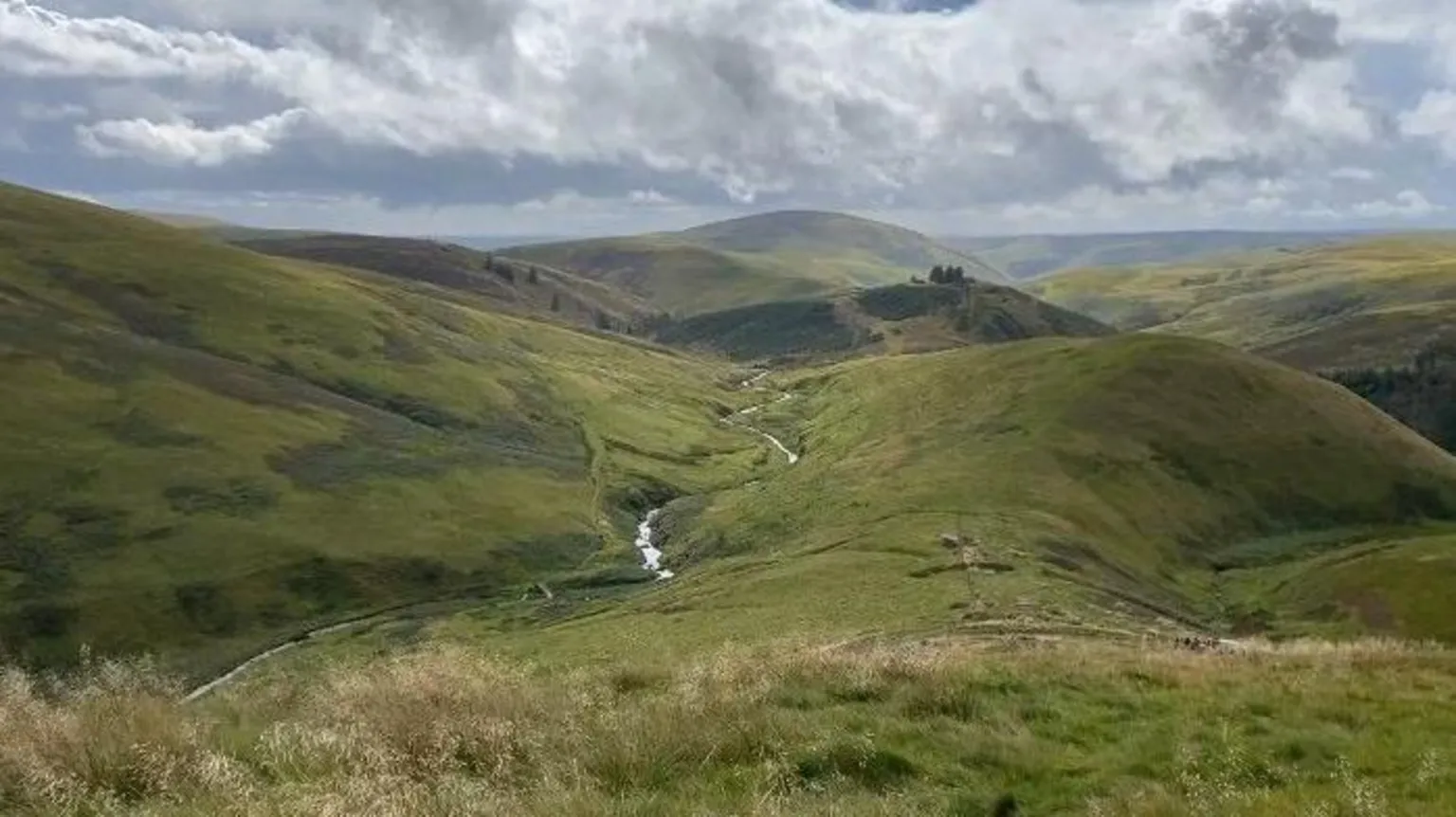 A vast green area of uplands stretches out in all directions with hardly a house to be seen. The sky is grey and blue