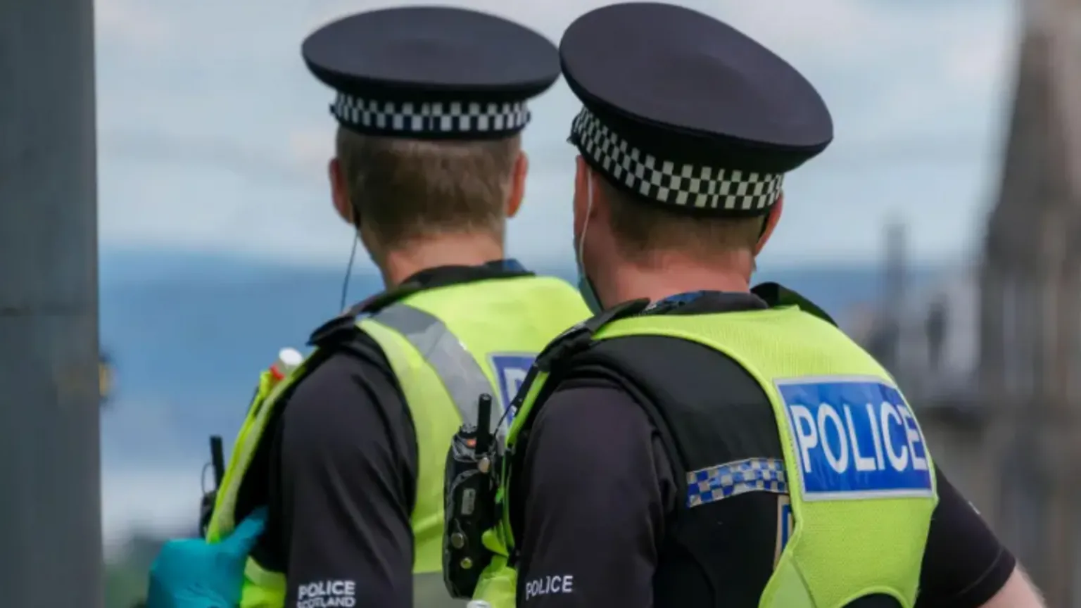  The back of two Police Scotland officers wearing their recognisable fluorescent yellow padded vests and black checked hats 