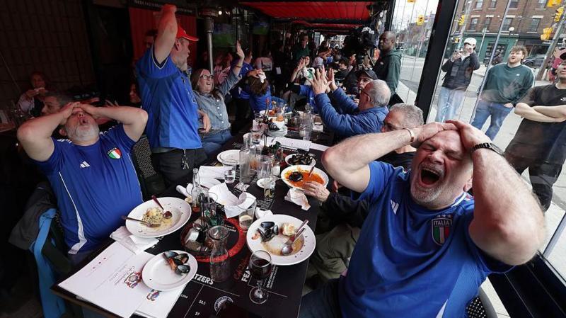 Italy fans sit at a table and have their hands on their heads