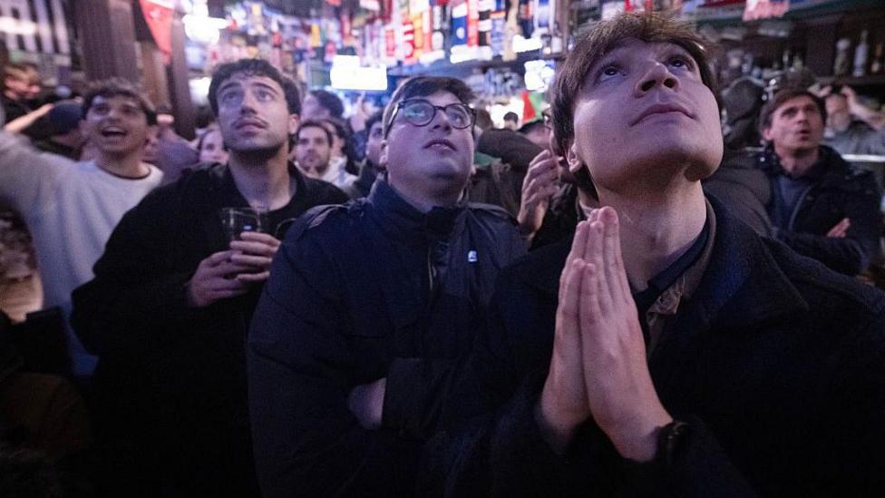 Italy fans watch football in a pub and one holds his hands together