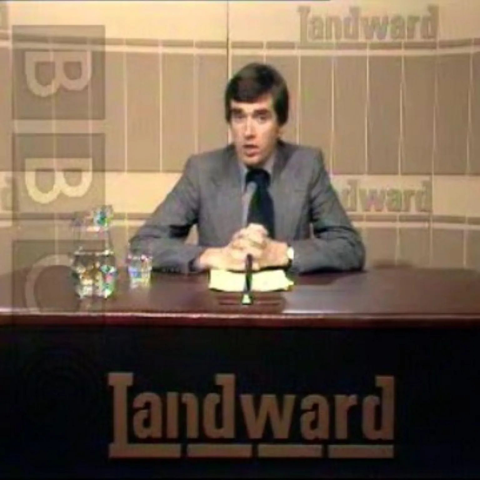 Ross Muir, the first presenter of Landward, dressed in a grey suit in a studio setting.