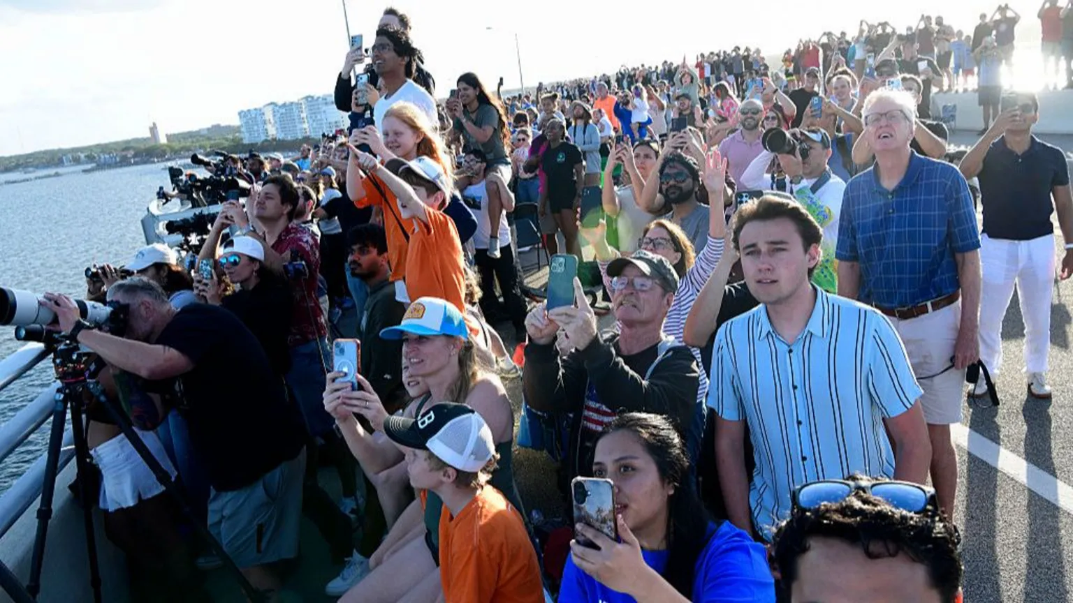 Gerardo Mora/ A group of people watches the launch, most holding phones or cameras up to the sky.