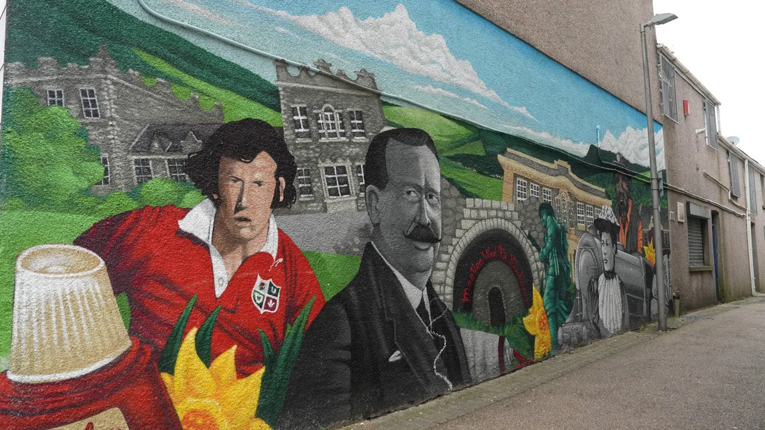 The mural includes a portrait of rugby player J. J. Williams, a bottle of nail varnish representing the former Revlon factory which was an important source of local employment, Maesteg's war memorial, and an image of Maesteg Community Hospital, built from funds raised by local mining families.
