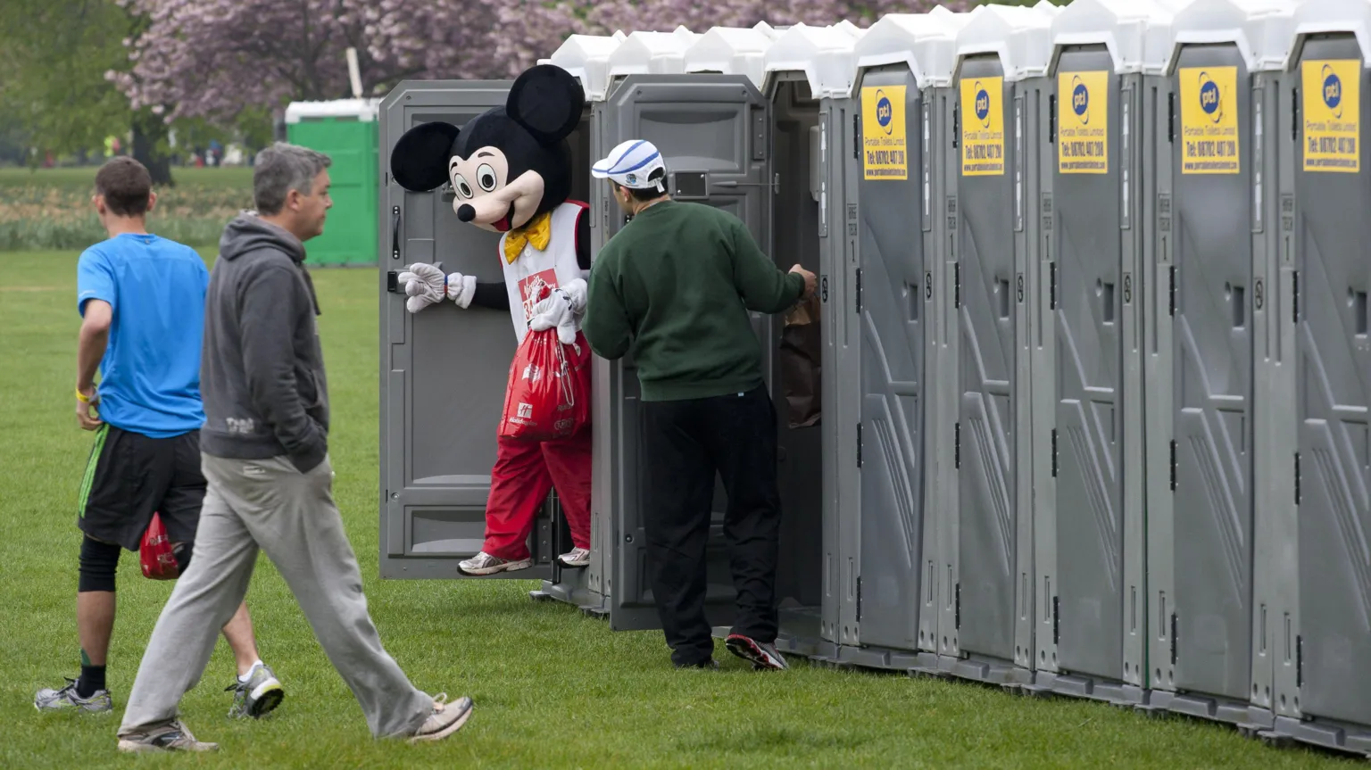  Fun runners at the start of the Virgin London Marathon - a man dressed in a Mickey Mouse costumes exiting a portable toilet 