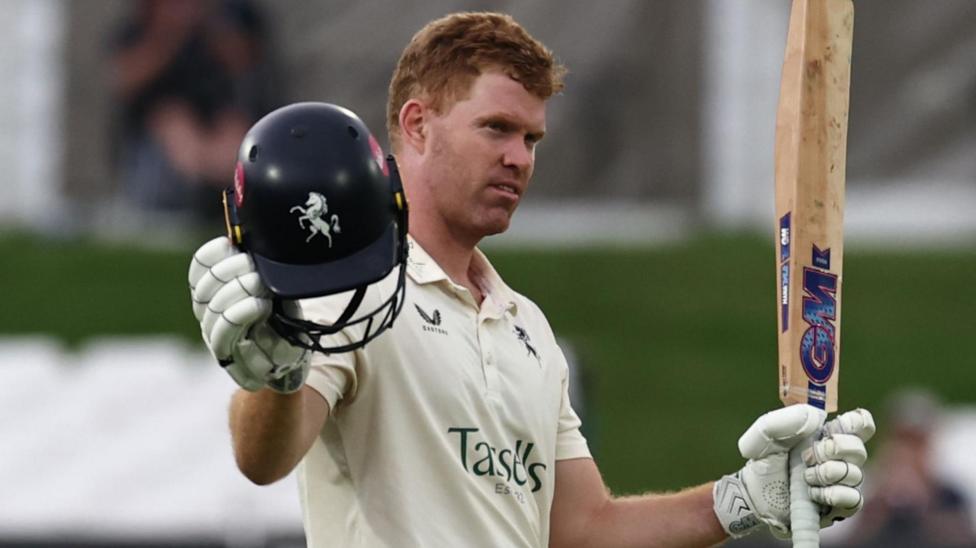 Kent's Ben Compton raises his bat in his left hand and blue Kent helmet in his right to acknowledge the crowd after scoring a century against Leicestershire at the Spitfire Ground on 30 July 2025