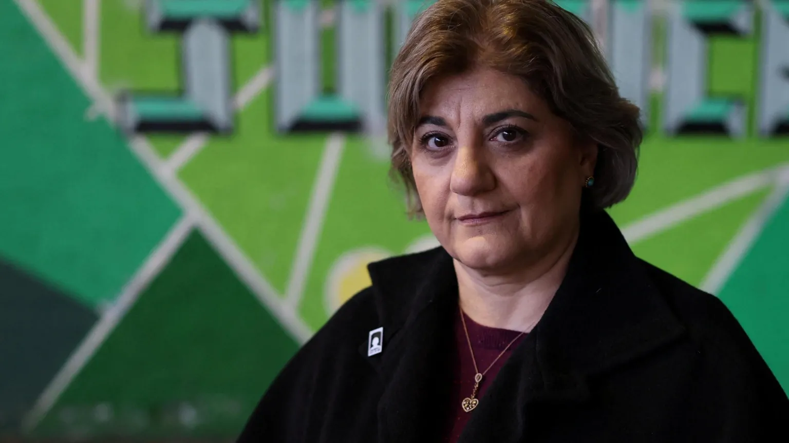  Kimia Zabihyan, a woman with short brown hair wearing a black fleece and maroon top, stands in front of a green mural that says 'justice'.