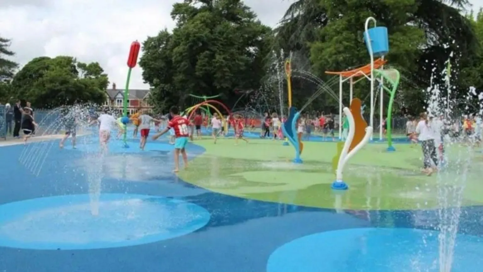 Cardiff council A splash pad at Victoria park with fountains and children playing. There are trees and houses in the background.