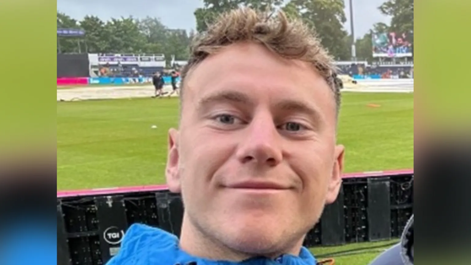 Dyfed Powys Police Adam pictured at a sports pitch with green grass behind him smiling at the camera in a blue jacket.