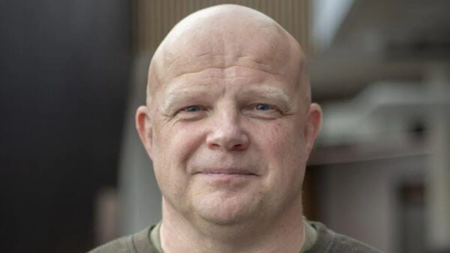 Andrew Bartlett Andrew Bartlett in the centre of the photograph smiling at the camera. He is middle aged, bald and has blue eyes. He wears a khaki long-sleeve t-shirt. 