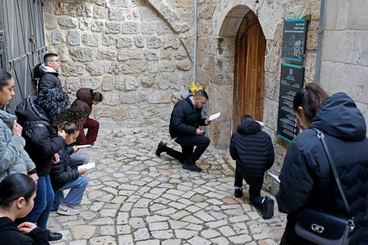 About a dozen Christian pilgrims kneel in prayer in front of the closed door of the Church of the Holy Sepulchre in the Old City of Jerusalem.