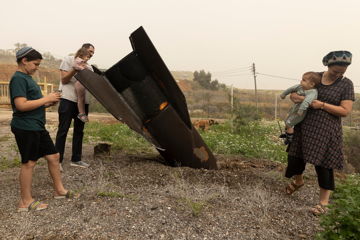 A family of five with small children stand near a missile lodged in the ground. 