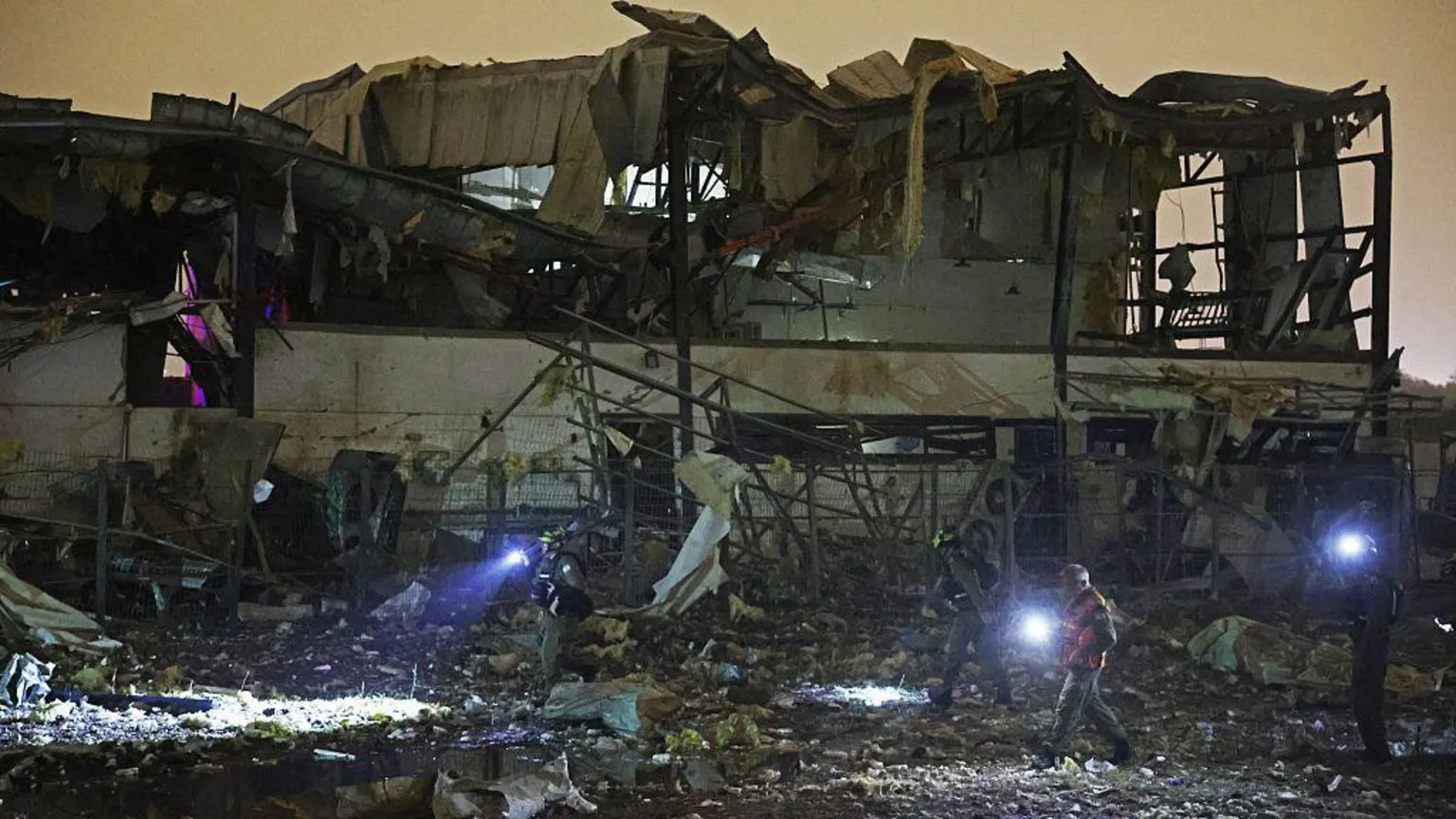  People walking around the ruined of an exploded building at night time with torches 