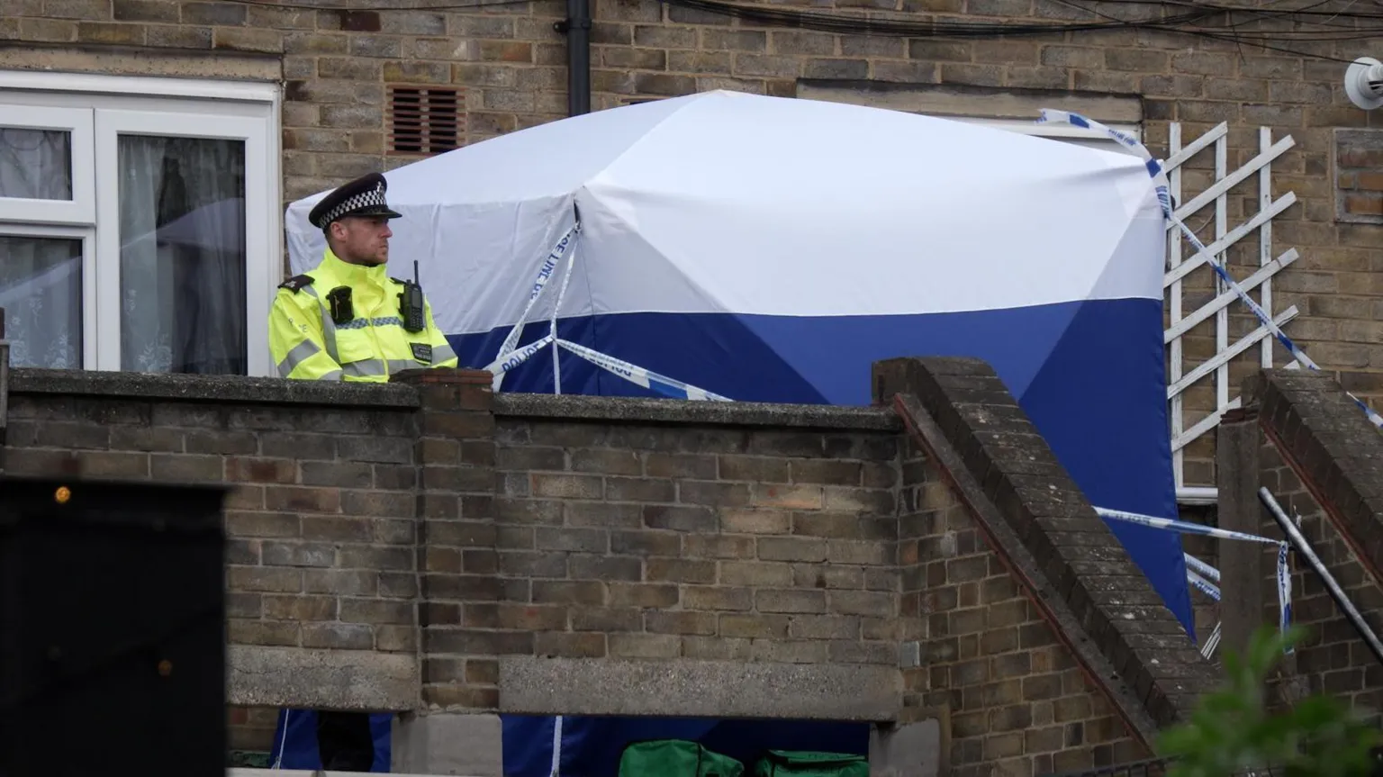 A blue and white police tent and a police officer standing outside a house