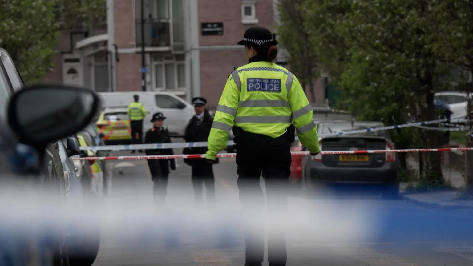  Several police officers standing in Lord Warwick Street, a residential road, and several lines of police tape.