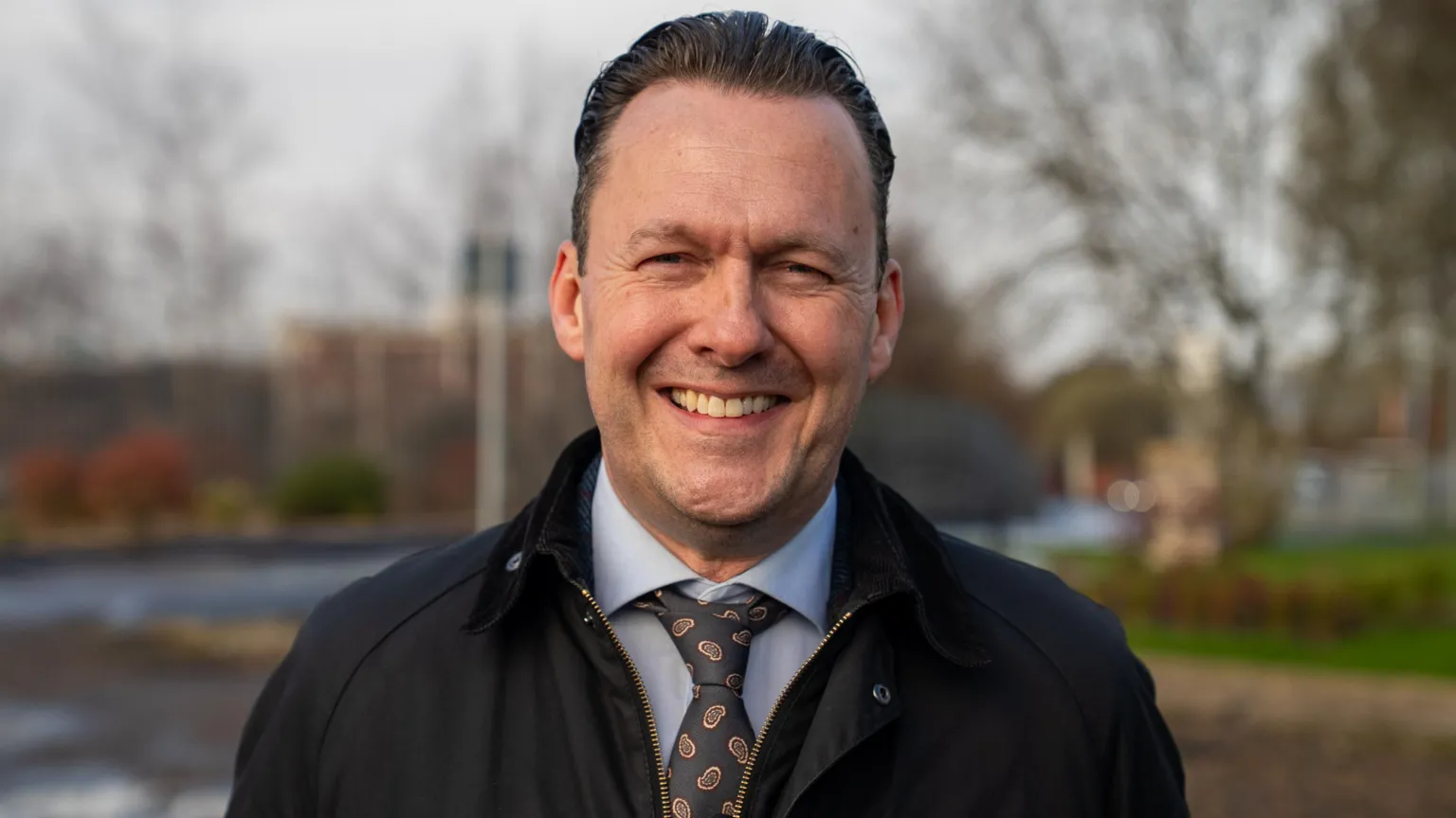 Russell Findlay smiles at the camera. He has a blue shirt on with a jacket on top. 
