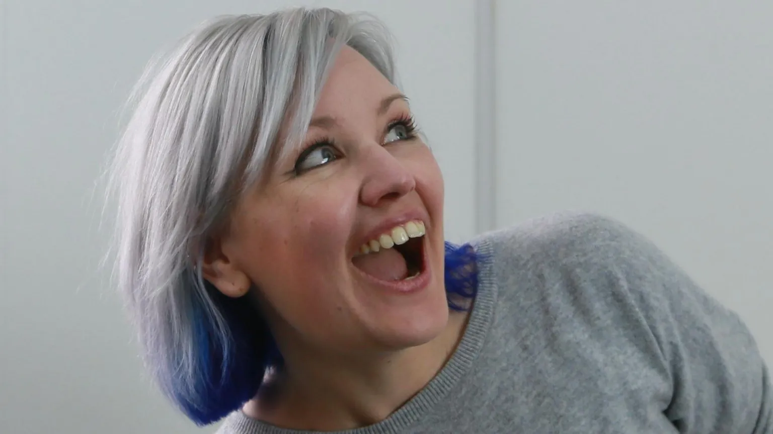 Kirsty Rigden A headshot of the CEO of FuturLab, Kirsty Rigden. She is smiling looking off the camera with her mouth open and has grey hair with purple strands. She is wearing a grey top.