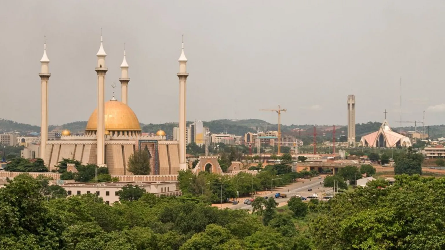 Abuja's main mosque and cathedral seen amidst a canopy of trees and cranes.