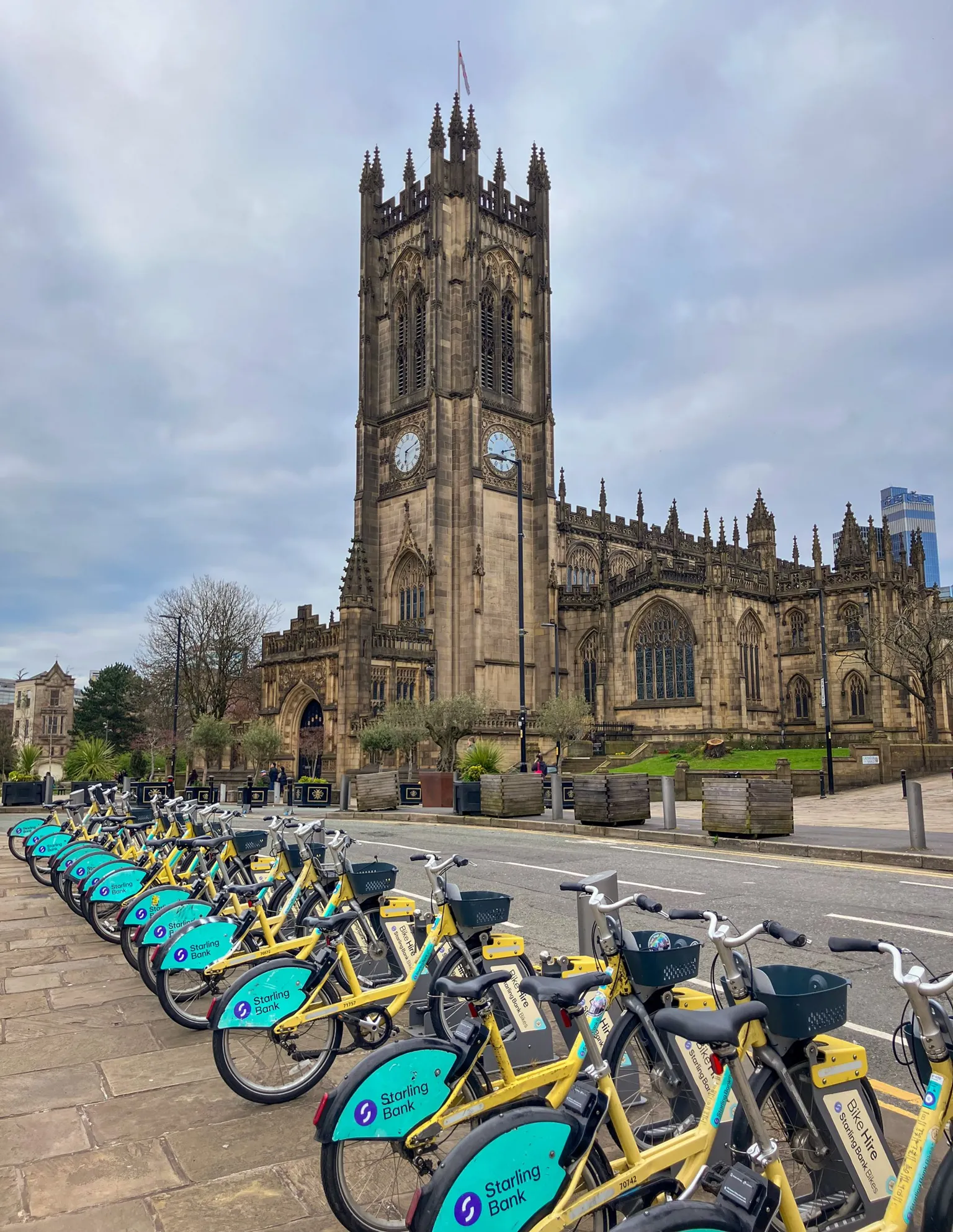 Rows of Starling Bank Bikes at a docking station in front of Manchester cathedral.