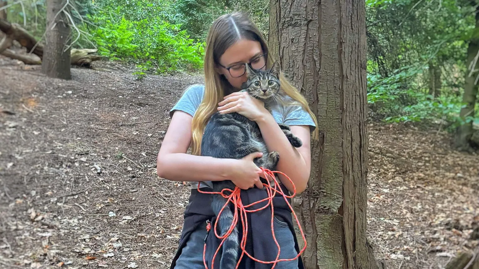 Alana Kestle Alana Kestle is holding Roo the tabby cat in her arms. Roo has wide eyes and Alana is kissing her head. Alana has long blonde hair and is wearing glasses. Behind the pair is a tree trunk and a forest.