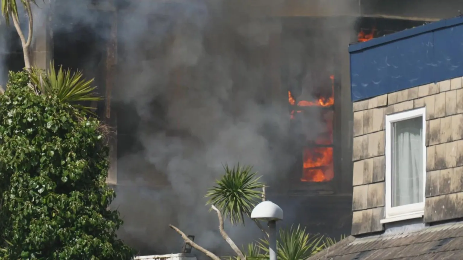 Naked flames behind a window of the hotel. There is thick black smoke inside and outside of the former hotel.