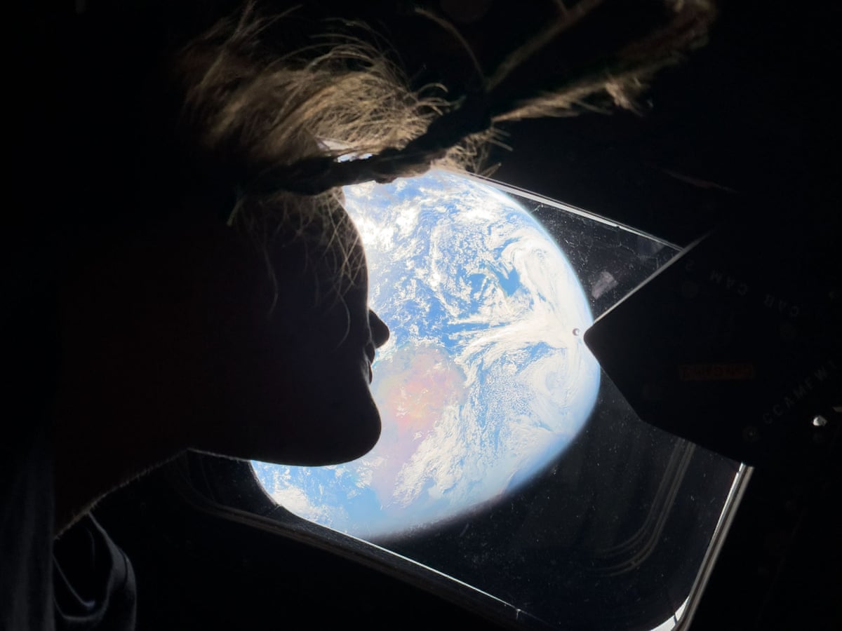 Silhouette of Christina Koch against an aerial view of Earth, from the vantage point of the interior of the Orion spacecraft
