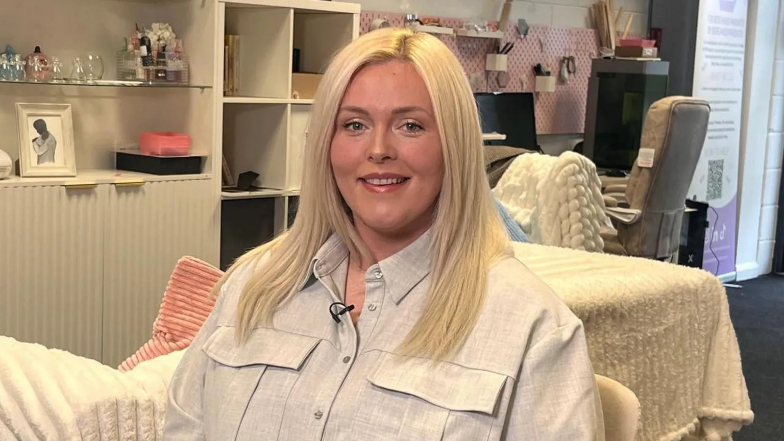 Megan is seated, wearing a grey shirt. She has long blonde hair. 