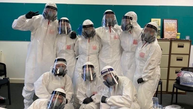 Myfyrwyr mewn siwtiau meddygol gwyn ac offer PPE