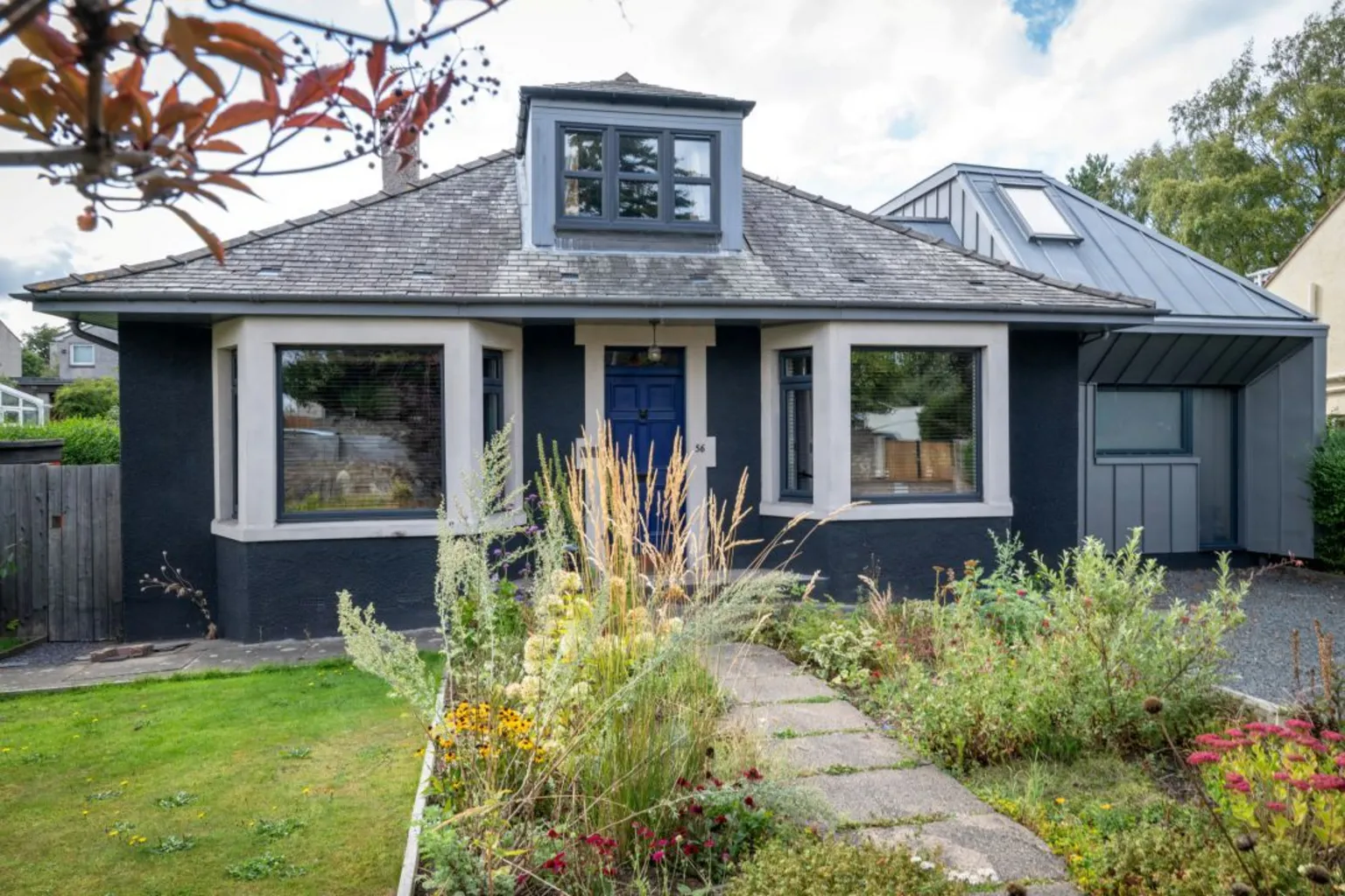 IWC Media Homegrown Hoose. A dark coloured bungalow with two bay windows at the front and a small garden.