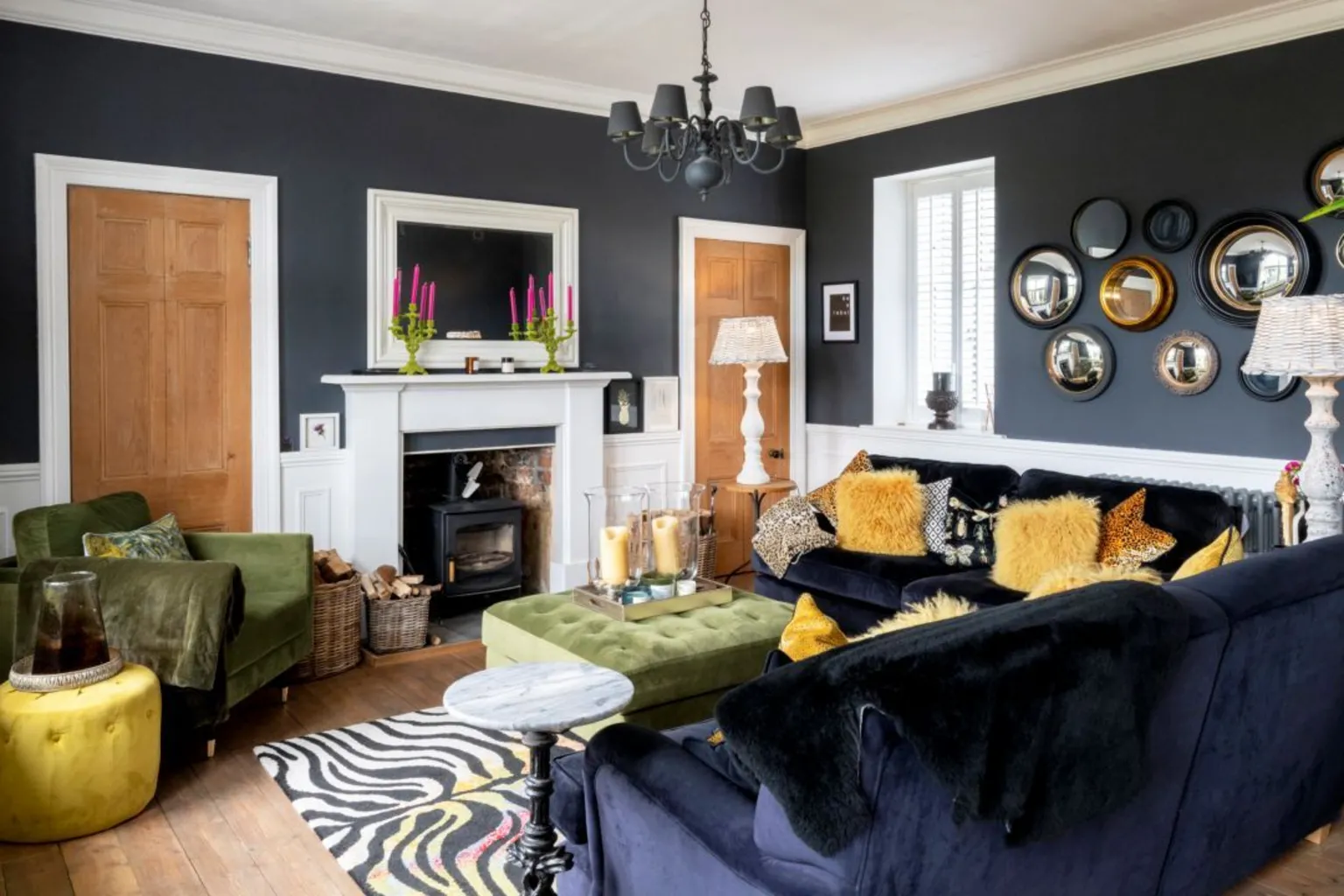 IWC Media Inside The Schoolhouse. The living room has black walls and dark coloured furniture, with a white fire place in the centre of the back wall.