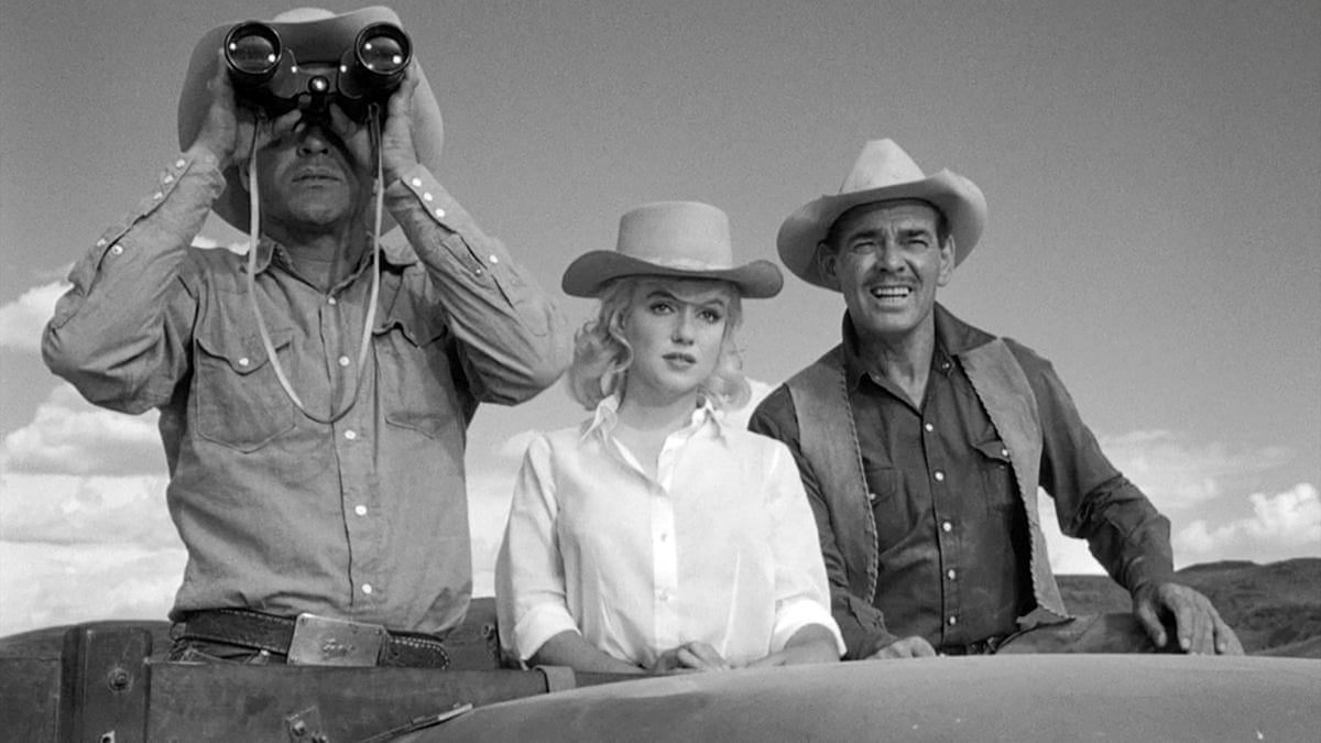 A black and white photo of Marilyn Monroe in The Misfits, standing next two male actors