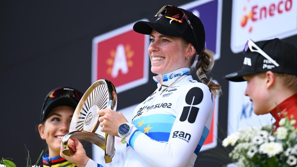 Demi Vollering holds the Tour of Flanders trophy, flanked by the second and third finishers
