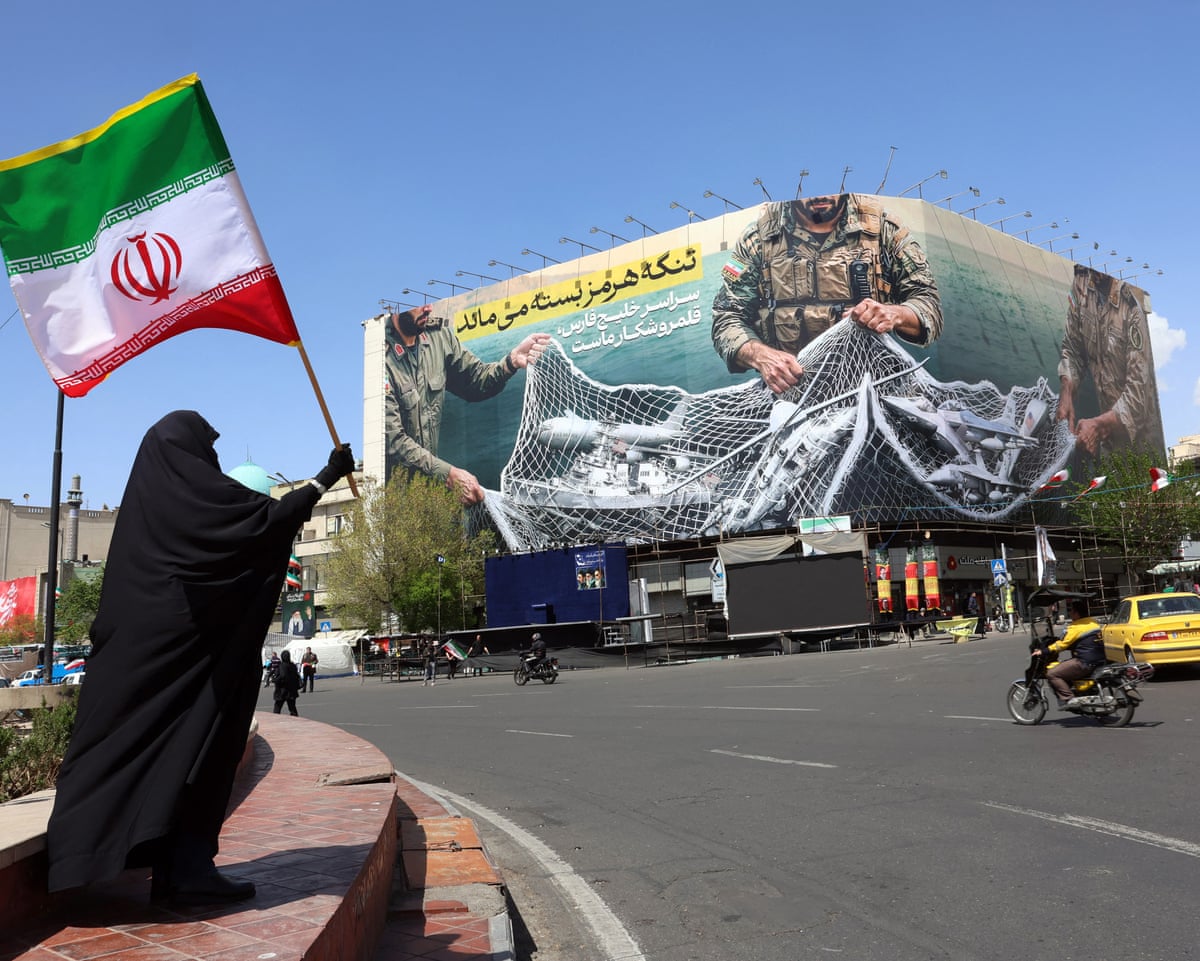A woman holds Iran's national flag while standing near a billboard with a sentence reading 'The Strait of Hormuz remains closed' at the Enqelab Square in Tehran, on 5 April 2026.