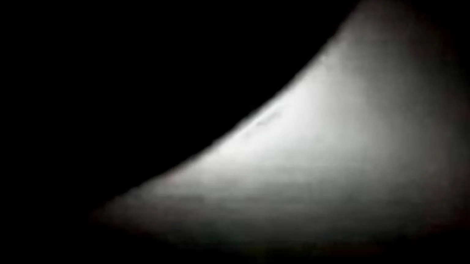 NASA Shimmering white light emerging from a portion of a dark circle in th eblackness of space.