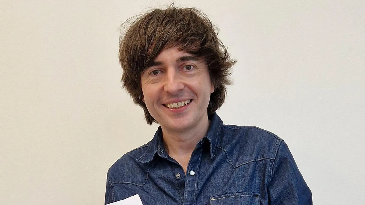 Danny Robins smiling wearing a denim shirt. It is a head and shoulders shot.