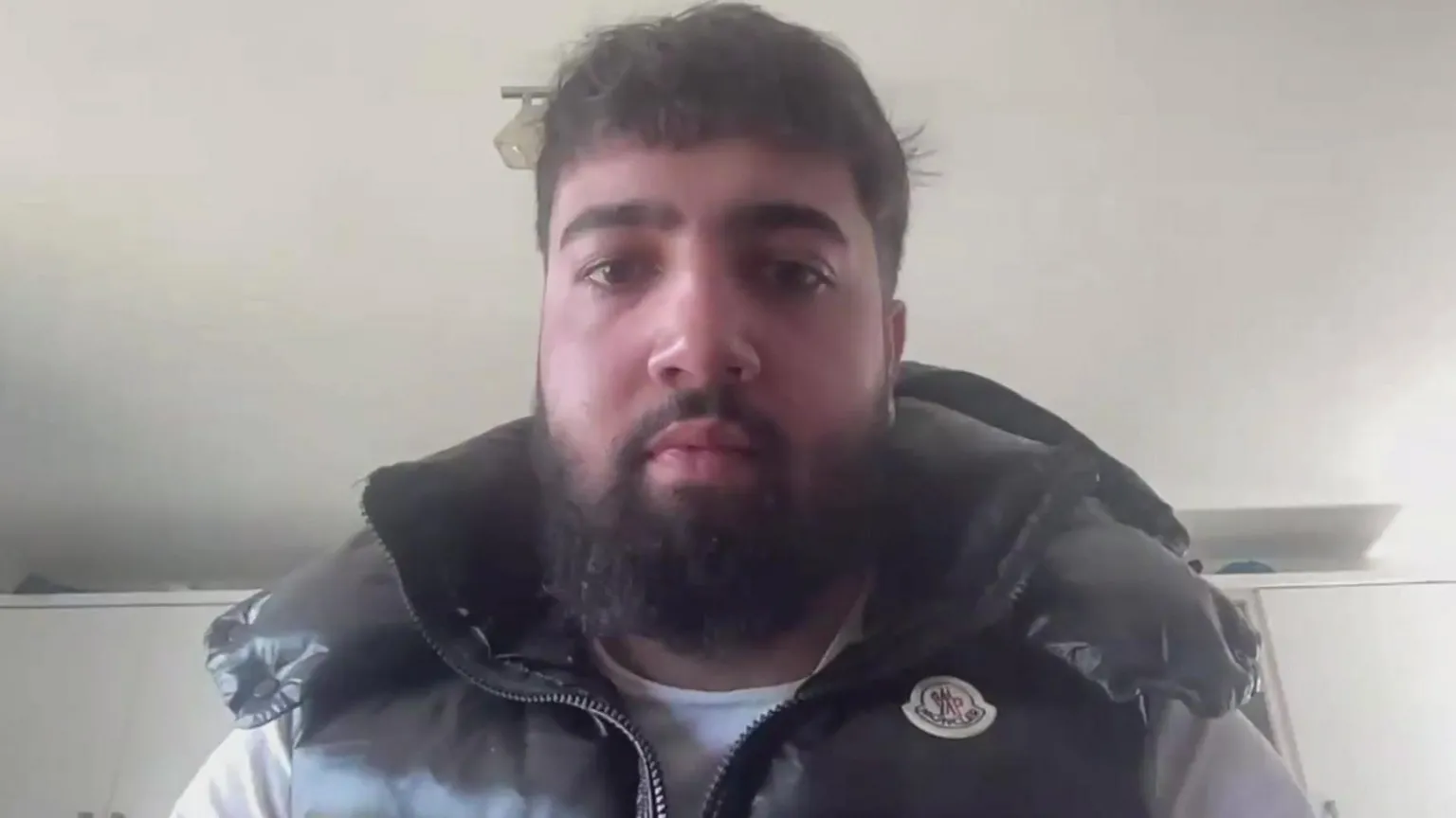 Zak Hanman has a dark beard and short dark hair. He is wearing a black coat.