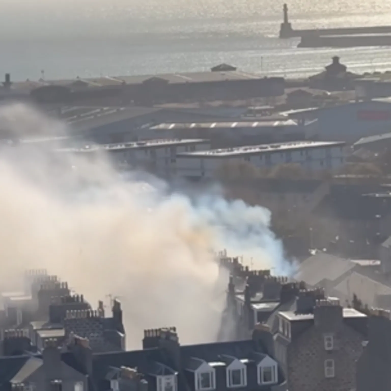 Fubar News Smoke billowing rooftops in Aberdeen city centre, the sea and a lighthouse can be seen in the distance.