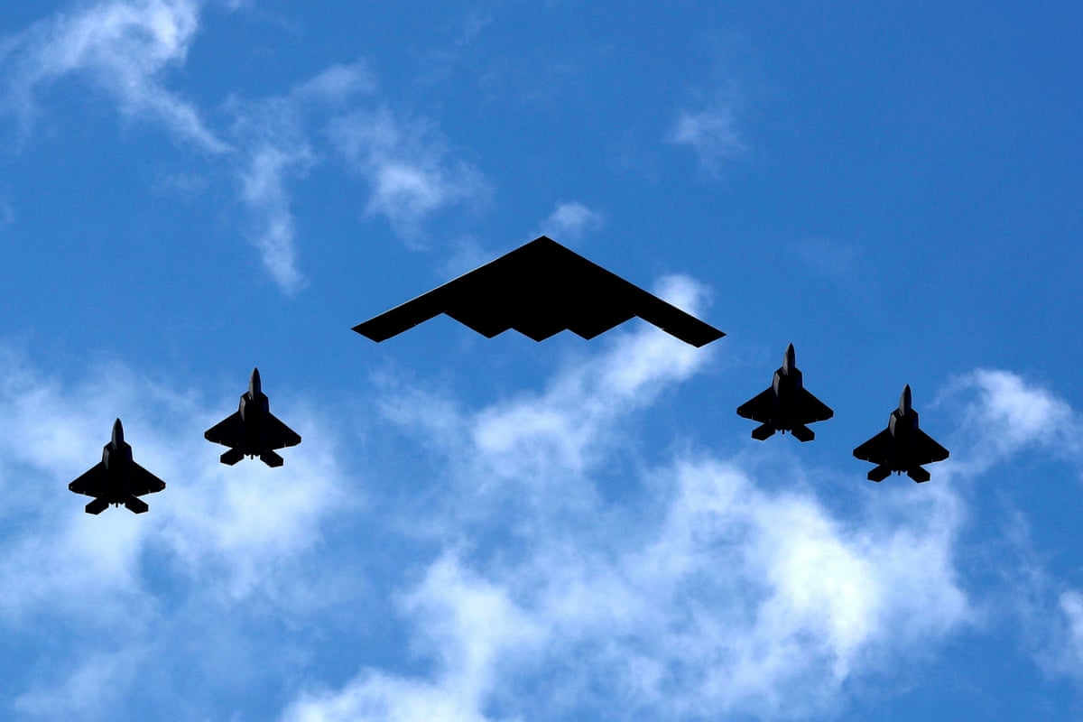 A US Air Force B-2 stealth bomber and four fighter jets silhouetted against a blue sky