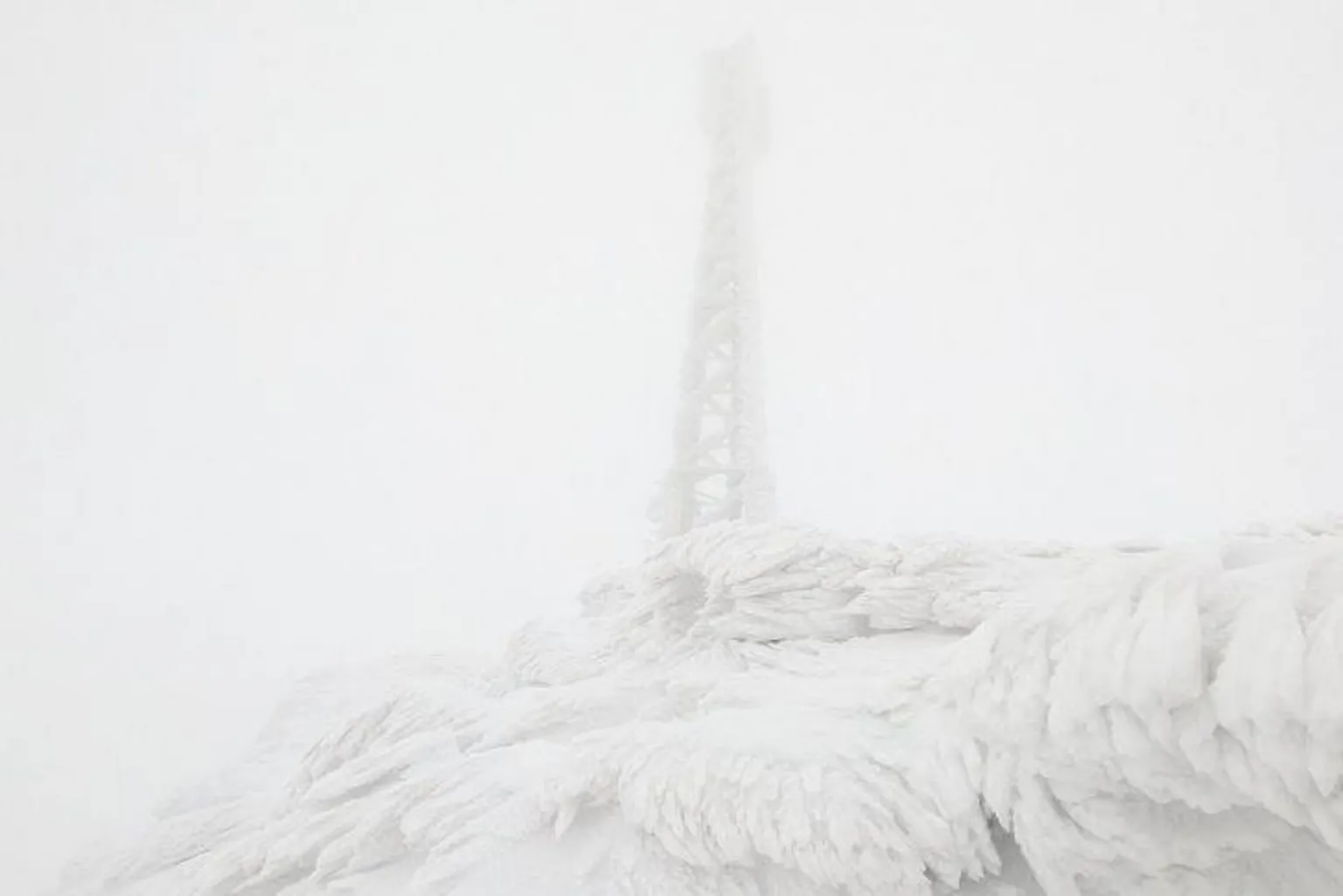 SAIS Glencoe The objects in the image are almost obscured by low cloud. The mast is caked in ice and rises above an area of ground covered in a meringue-like covering of ice.