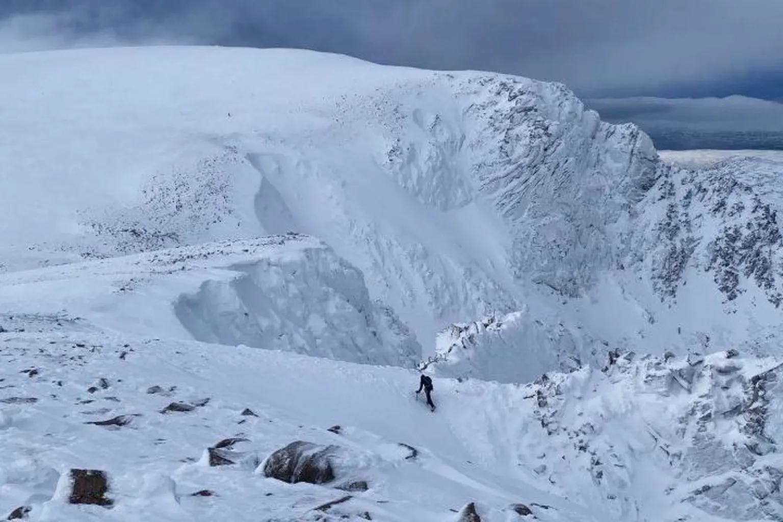 SAIS Northern Cairngorms A climber walks up a snow-covered slope in the Northern Cairngorms. He is dwarfed by a snowy mountain rising before him.