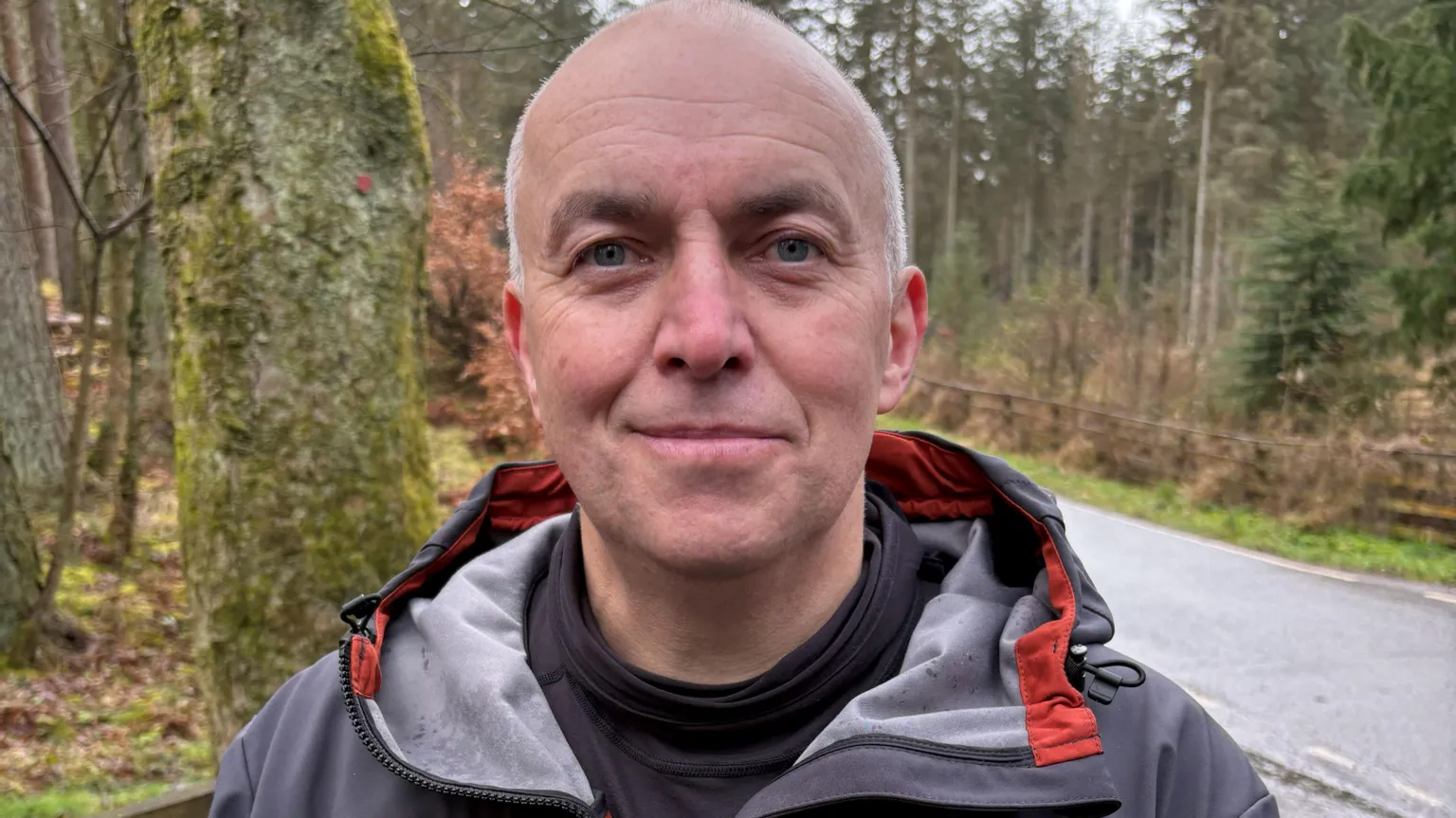 Steve Band - Man standing outdoors on a woodland path, wearing a grey and orange jacket.