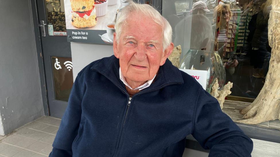 Alfor Jones yn eistedd gyda phaned yn Aberaeron 