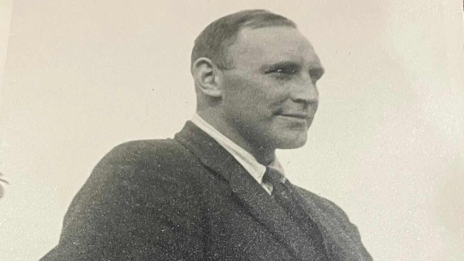 A black and white image of Blair 'Paddy' Mayne. He is looking away from the camera and is wearing a black blazer, white shirt and tie.