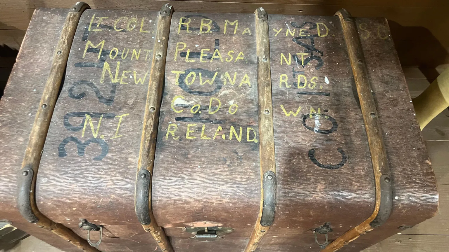 A vintage brown trunk with Blair Mayne's name and address in Newtownards, Northern Ireland written on it in yellow paint.