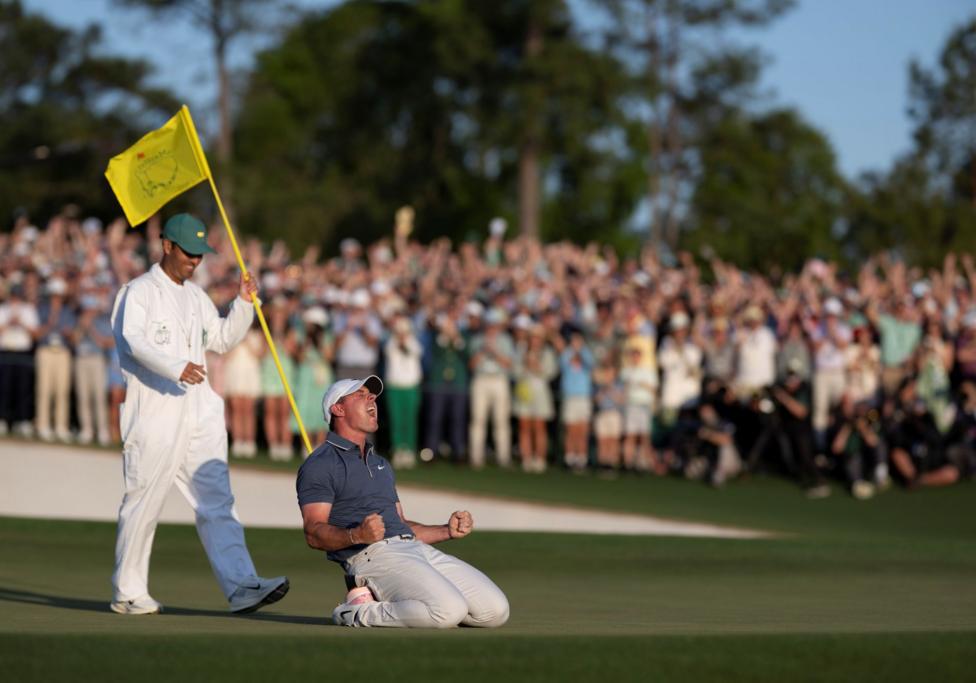 Rory McIlroy, on his knees on the 18th green at Augusta National, lets out a huge roar as he celebrates winning the Masters in 2025 to complete the career Grand Slam. His caddie, Harry Diamond, is stood behind him