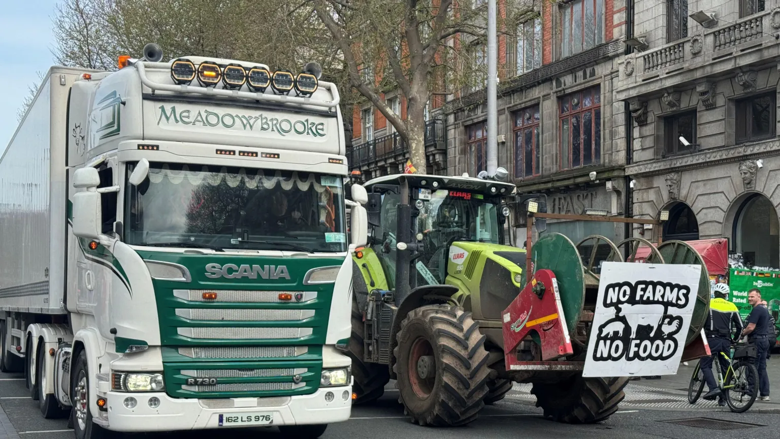  A lorry and a tractor are parked in the middle of O'Connell Street in Dublin. A sign on the front of the tractor says: 