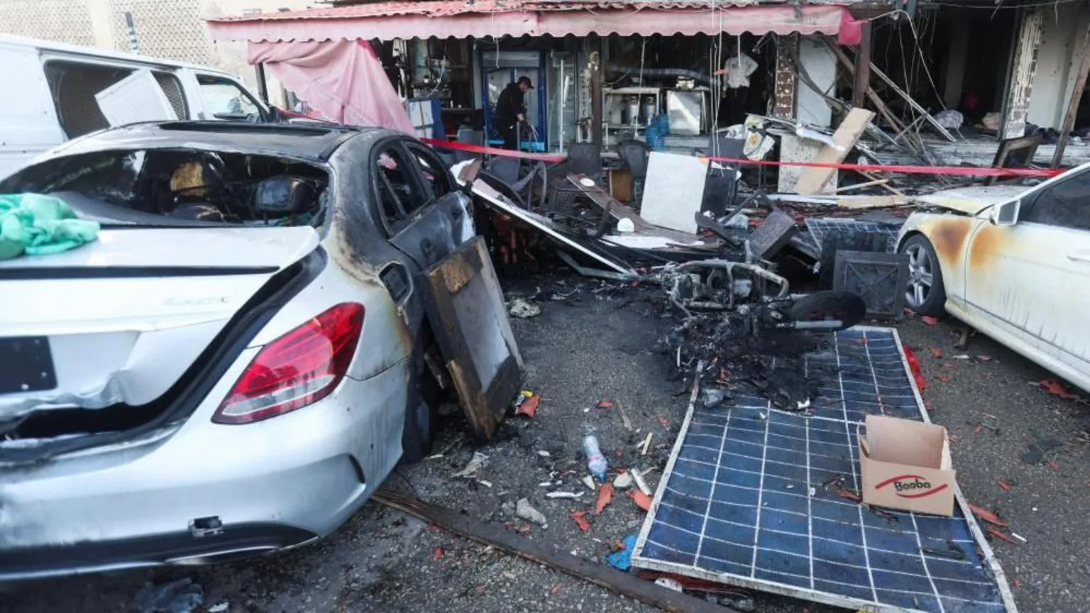 Damaged cars and a cafe which has a single man inspecting the aftermath of the strike